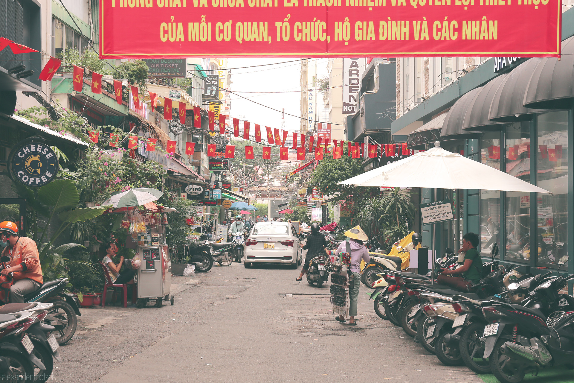 Foto von A bustling alley in Saigon alive with flags, scooters, street vendors, and daily city pulse in the heart of Ho Chi Minh City, Vietnam.