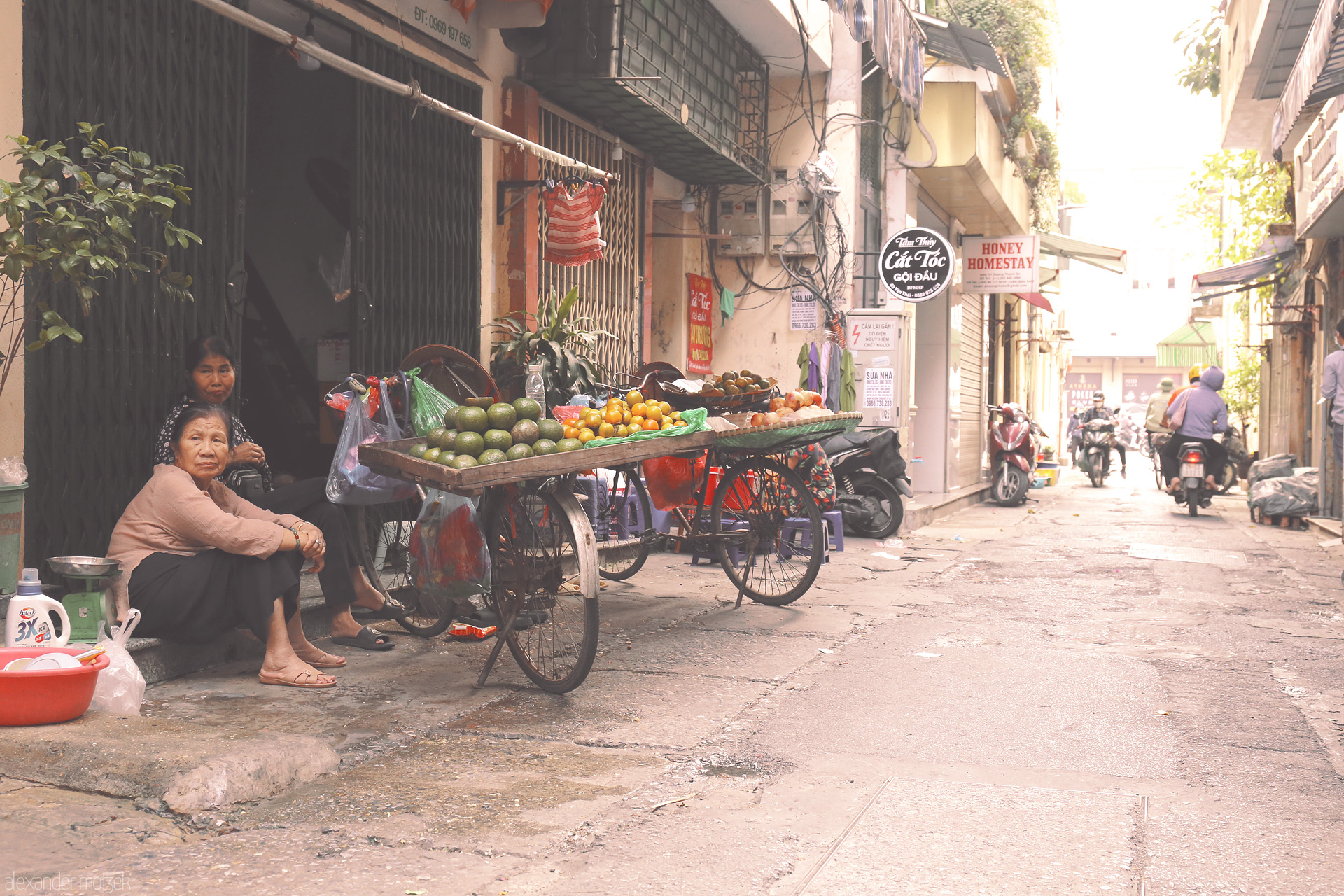 Foto von A quiet street scene in Phuong Cua Dông, Hanoi—fruit vendors, scooters, and morning life glow in soft sunlight.