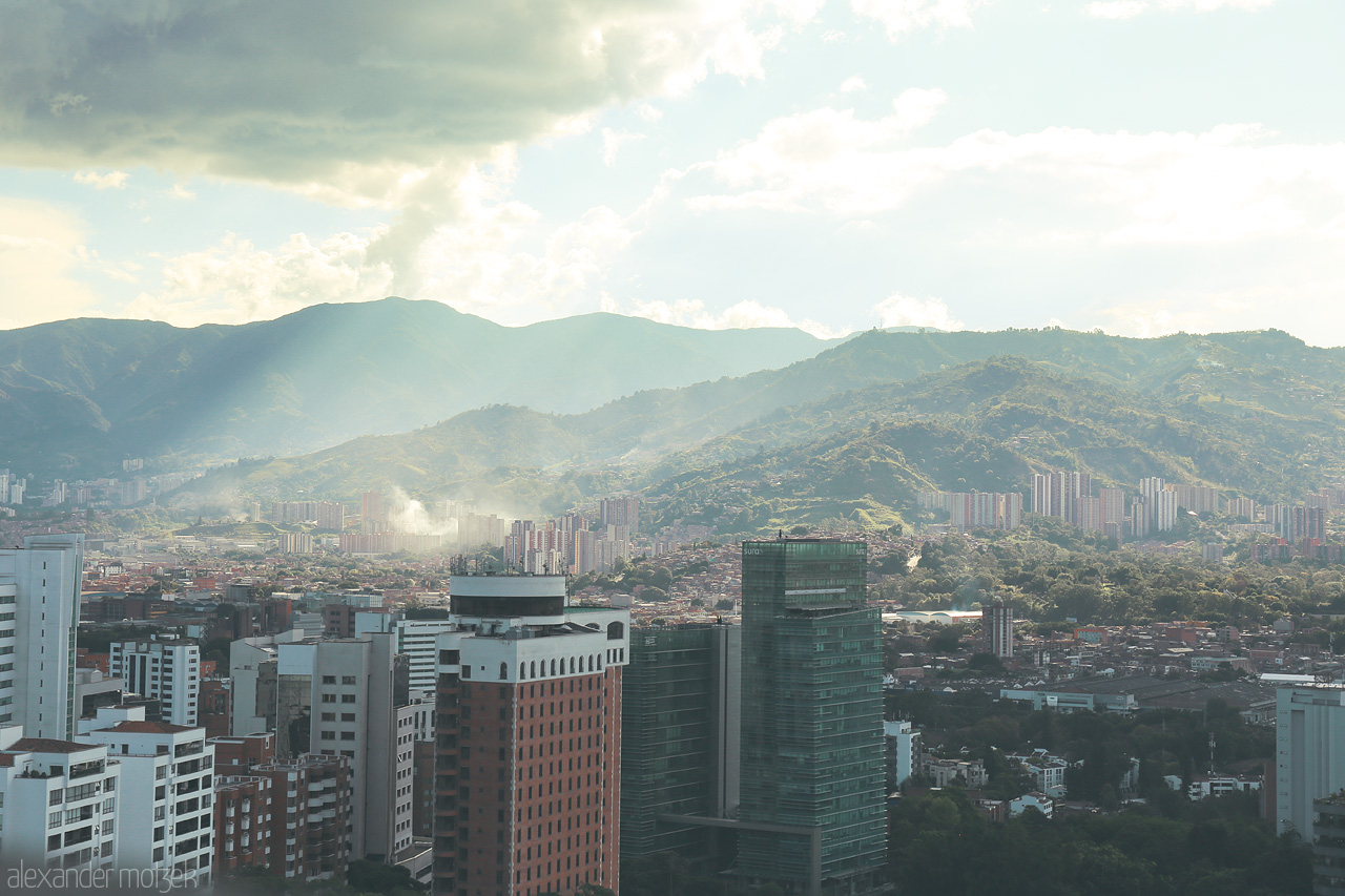 Cielo y Montañas Foto von A stunning view of Comuna 14 - El Poblado in Medellín, Colombia, with cityscape merging into the verdant Andean mountains under a dramatic sky.