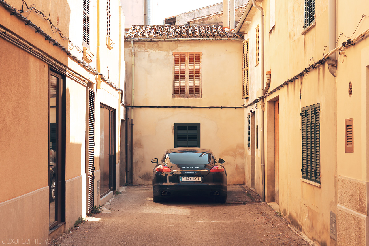Balearic Panamera Foto von A sun-soaked alley in Pollença, Mallorca, graced by terracotta rooftops and a solitary parked car.
