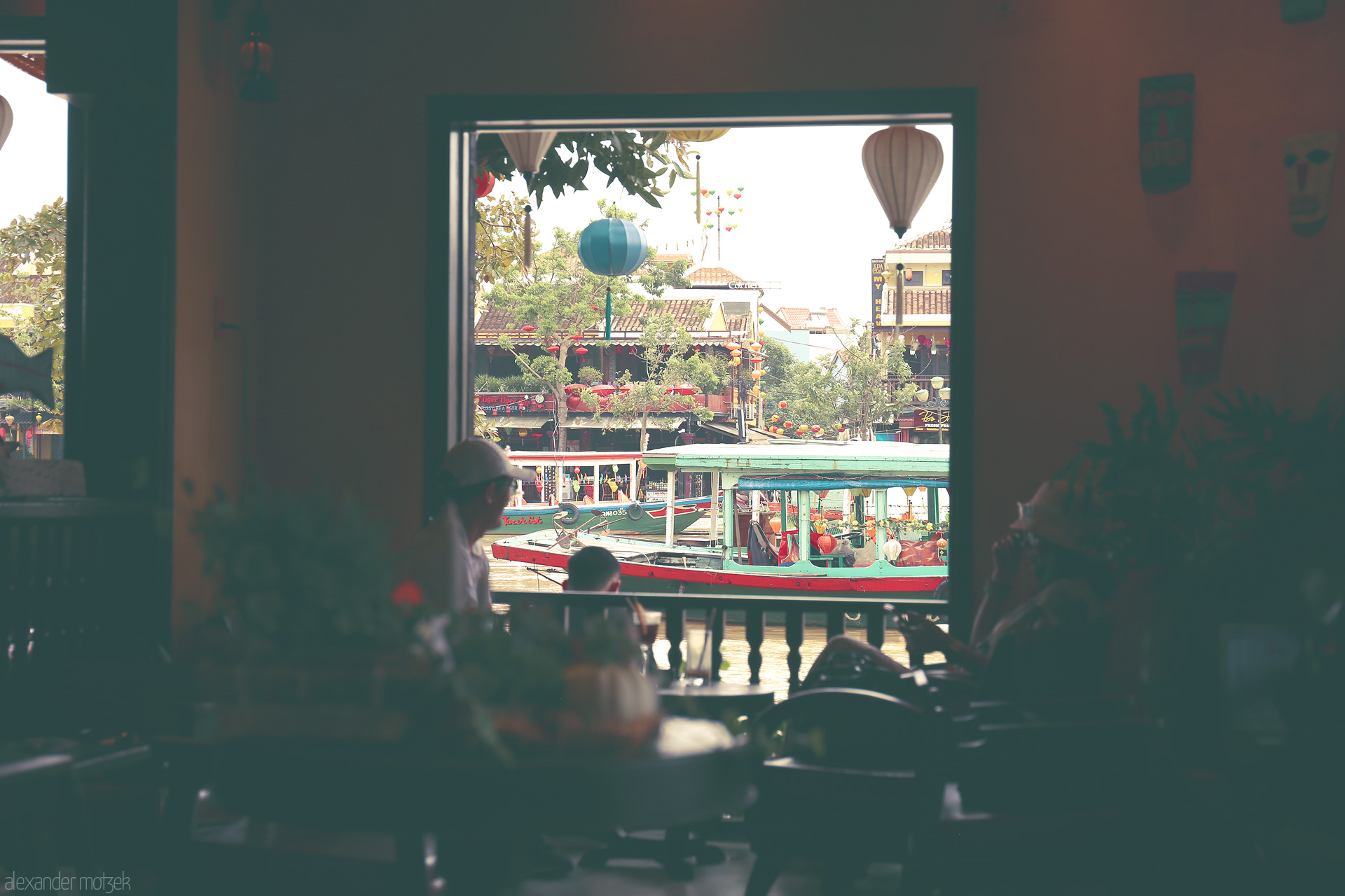 Foto von A tranquil café window overlooks Hoi An's old town, colorful boats, and floating lanterns on the Thu Bon River.