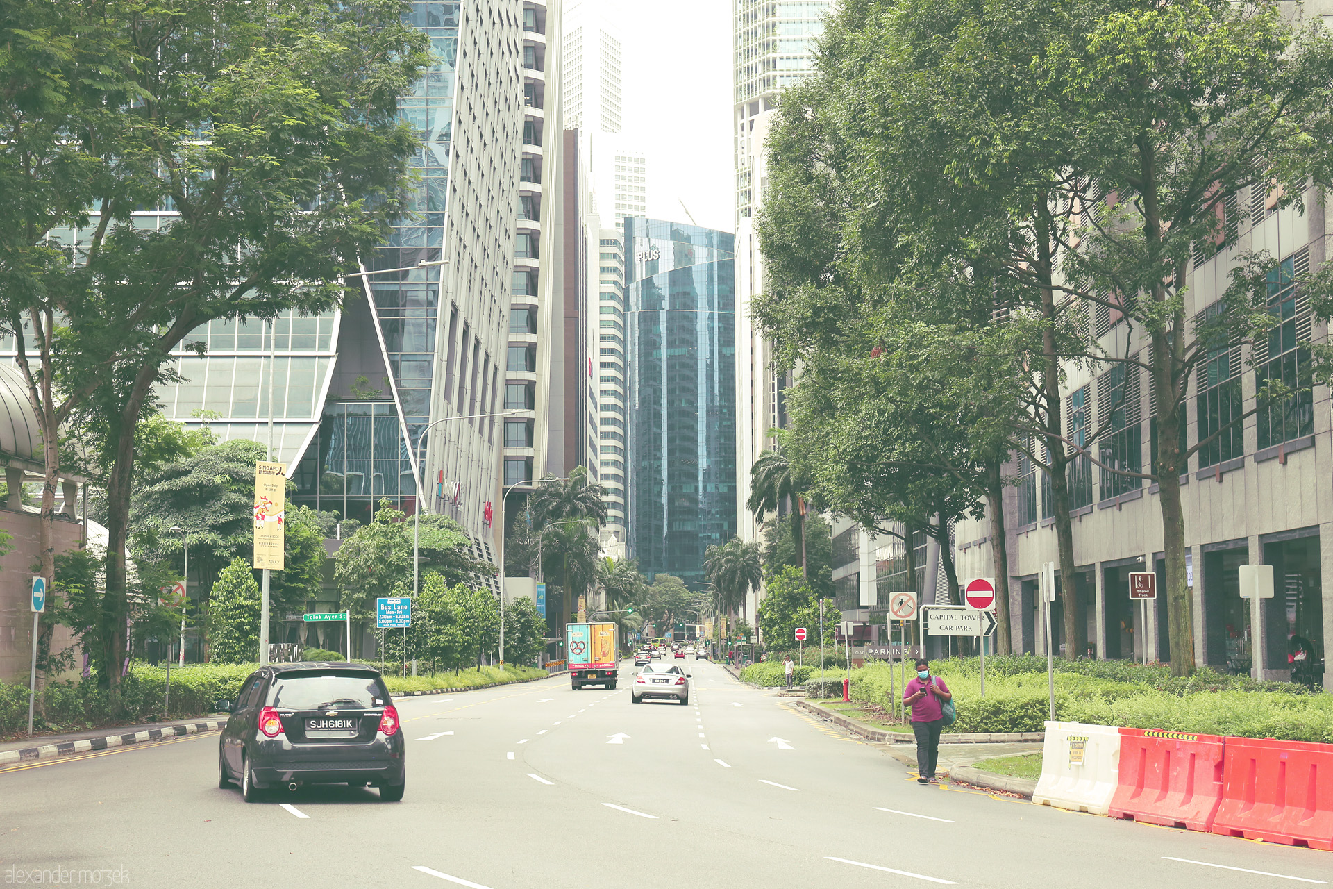 Foto von A tree-lined street gently curves into Singapore’s CBD, where glass towers rise above tropical greenery in a tranquil cityscape blend.