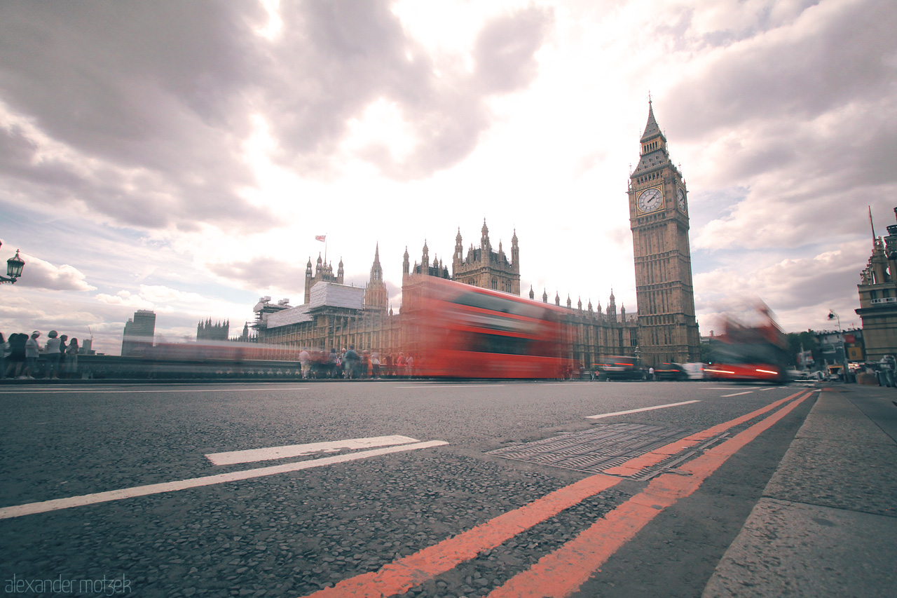 Timeless London Whirl Foto von Big Ben and busy red buses, captured in motion on Westminster Bridge under a cloudy London sky.