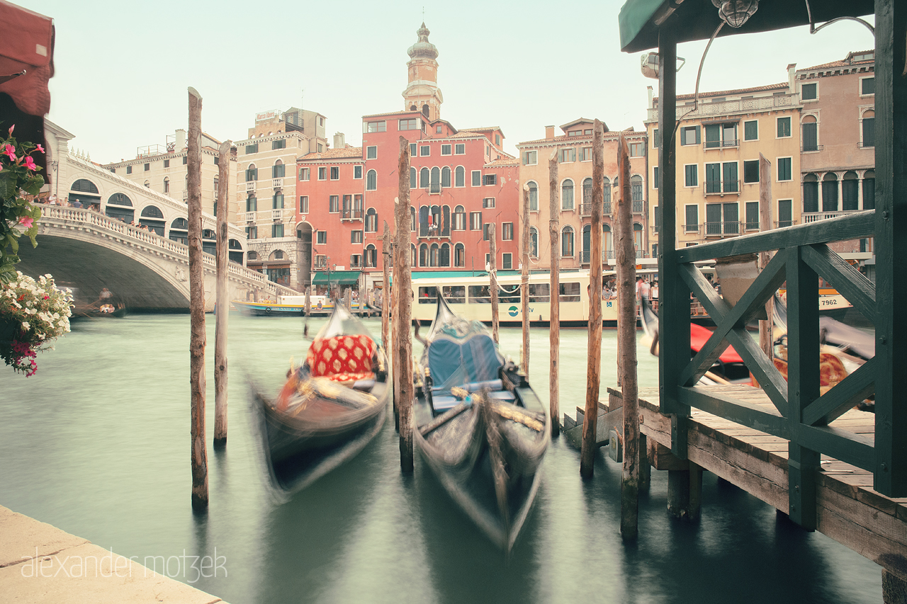 Gondole in Movimento Foto von Blurred gondolas floating by a vibrant Venetian canal under an arching bridge; a still moment in dynamic Venice.