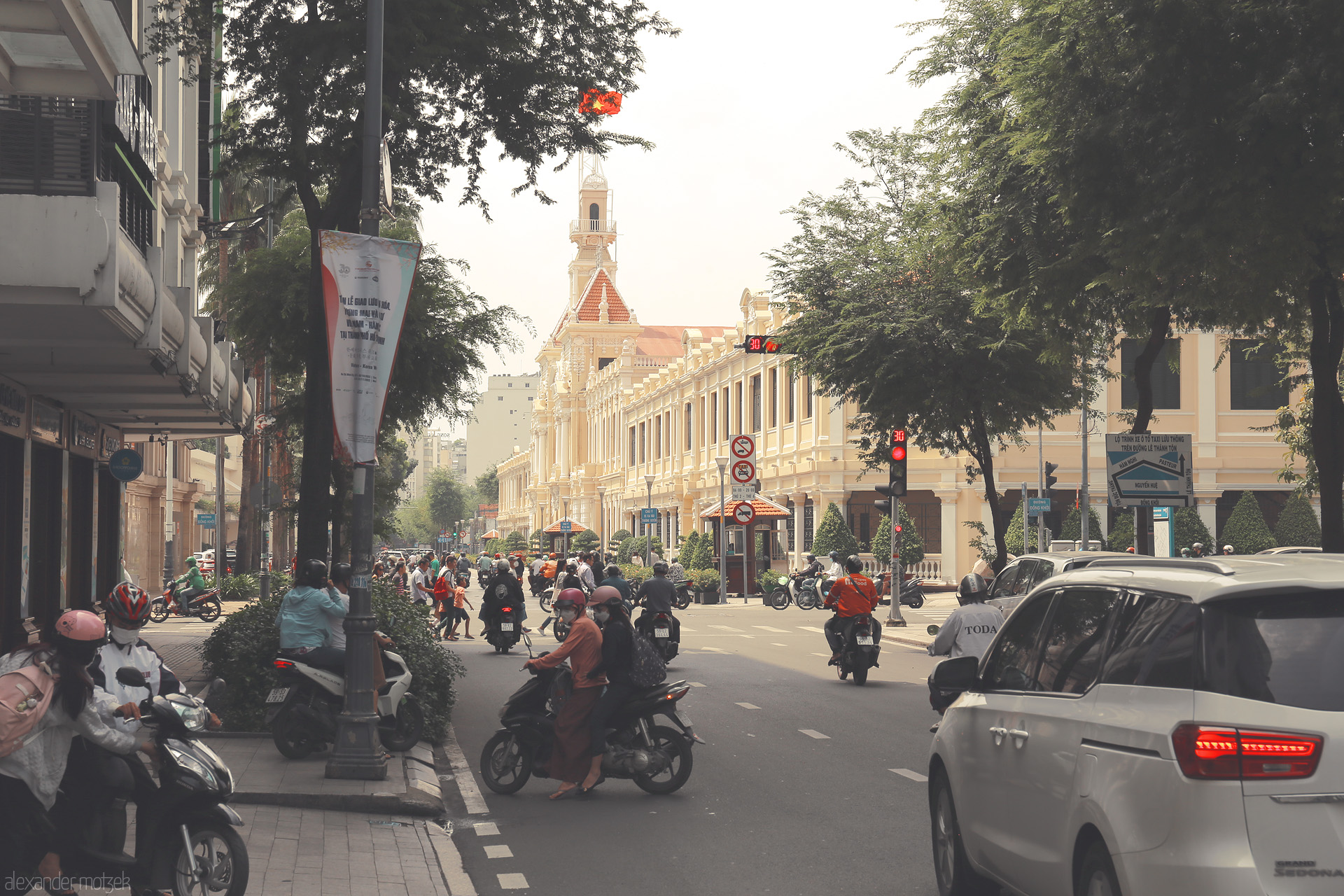 Foto von Bustling motorbikes and colonial charm: a sunlit street scene at Ho Chi Minh City Hall, Saigon's beating heart.