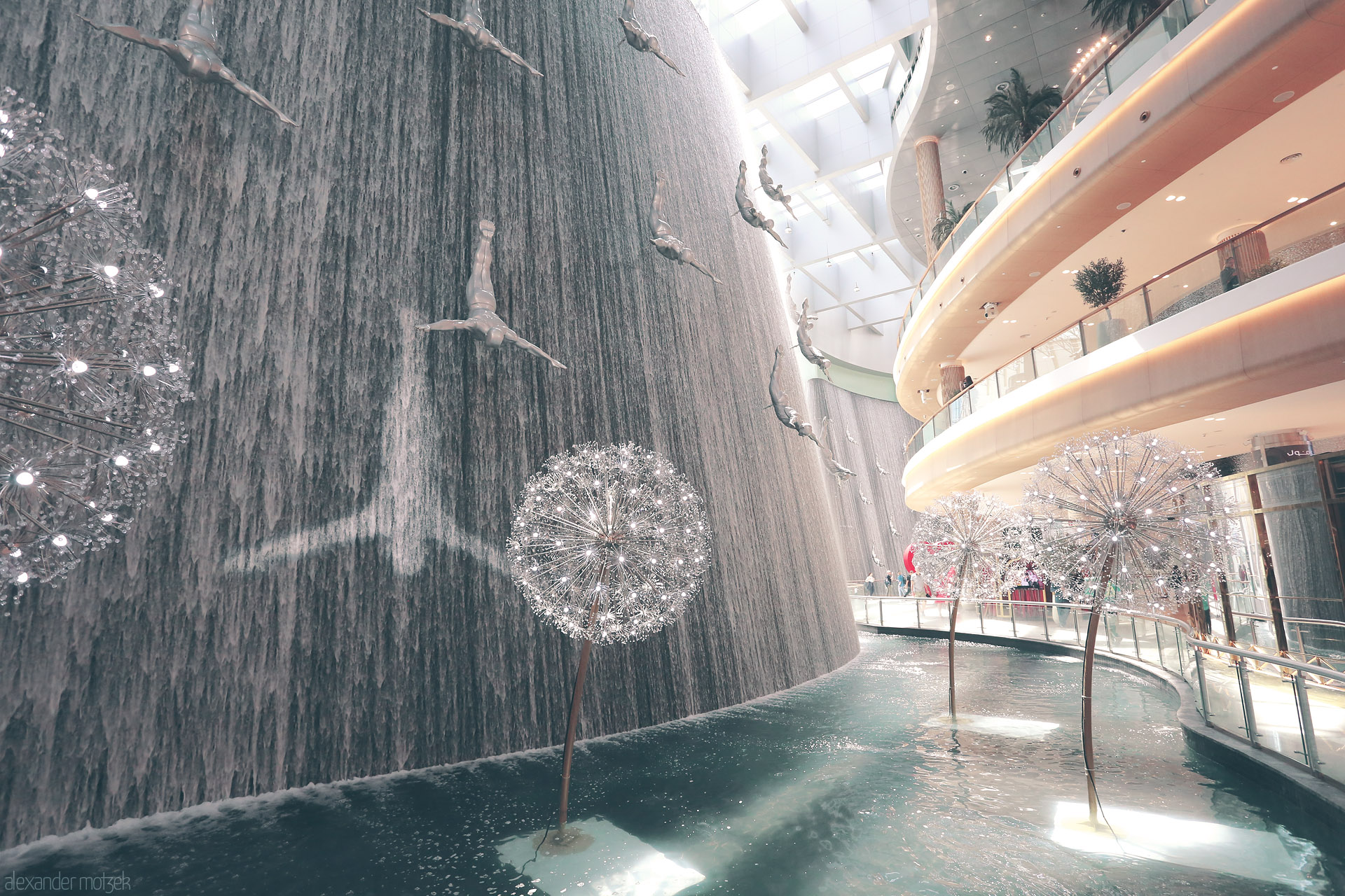 Foto von Divers soar through a cascading waterfall inside Dubai Mall, where art and water meet under the light of modern dandelions.