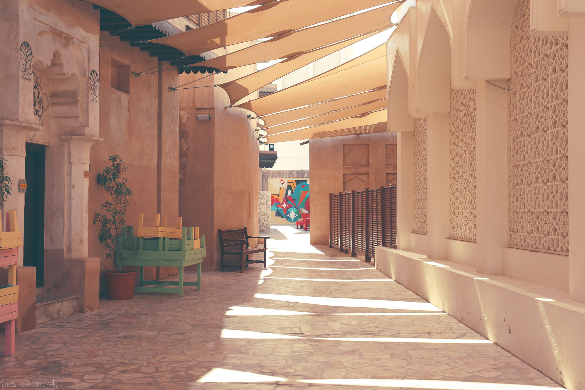 Al Seef Shadowscape Foto von Golden rays dance on heritage walls and pastel benches in a quiet Al Seef alley, Dubai, where tradition meets vibrant street art.