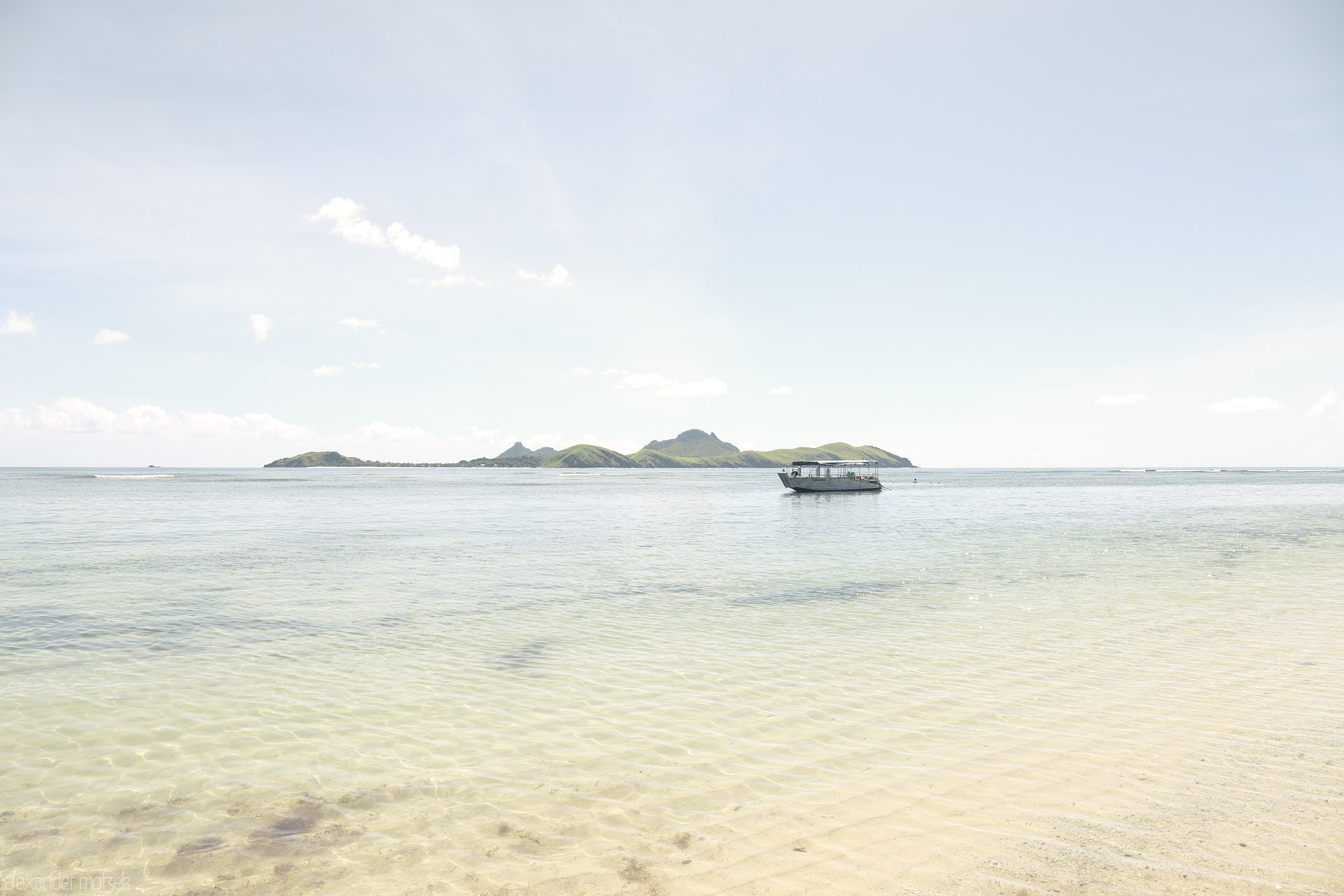 Foto von Crystal shallows and a small boat drift before green islets on Tokoriki’s calm lagoon, Fiji.