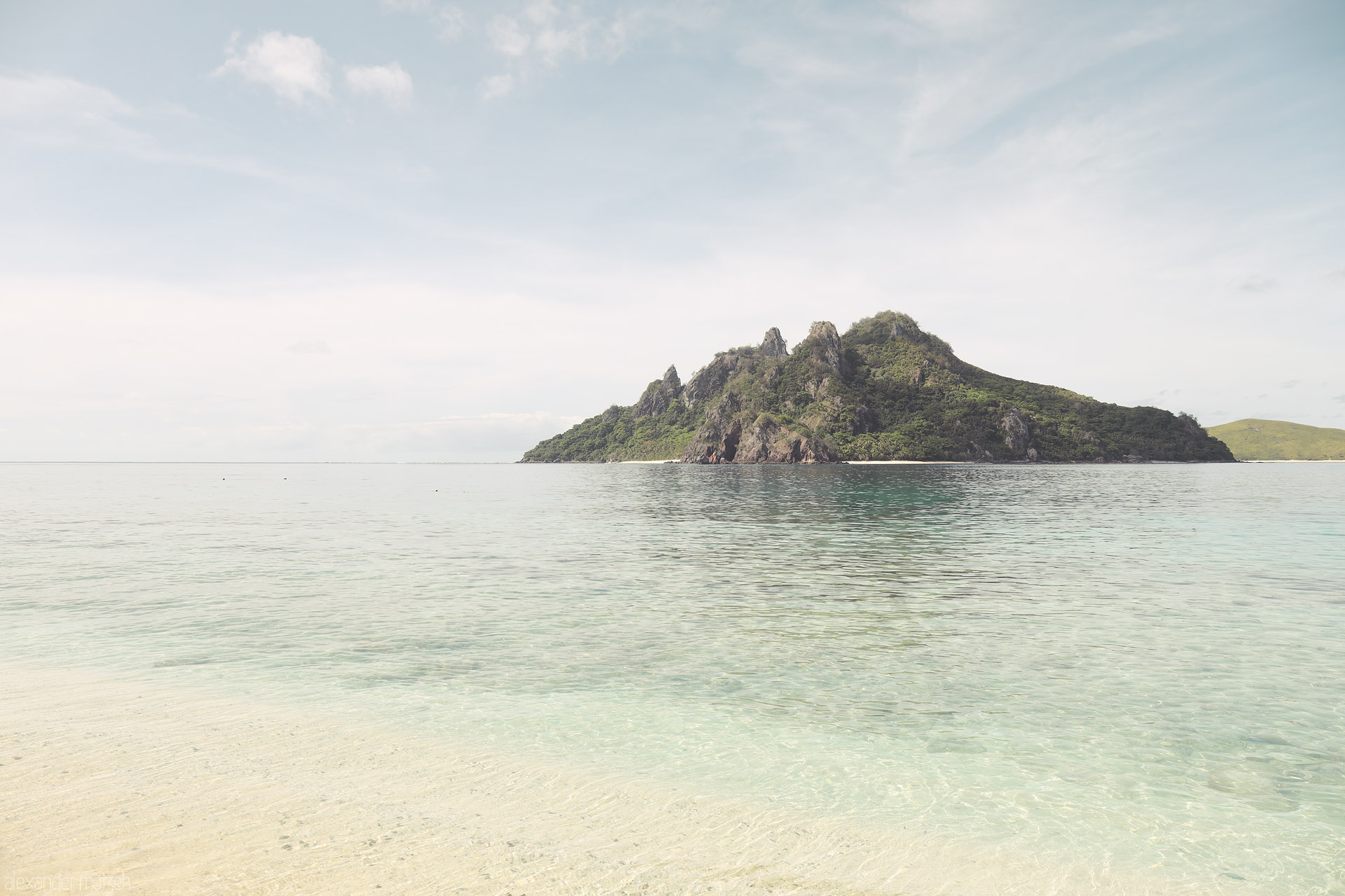 Foto von Glass-clear shallows and a lone green isle in Monoriki, Fiji—Castaway’s filming island—floating under a soft Pacific sky.
