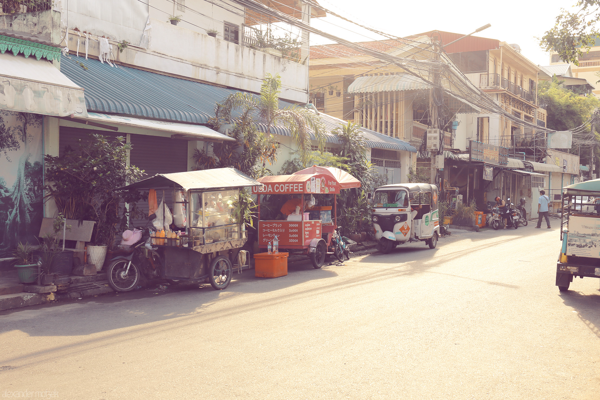 Foto von Golden morning light falls on street vendors and tuk-tuks in Kandal, Cambodia—a tranquil slice of daily life and coffee culture.