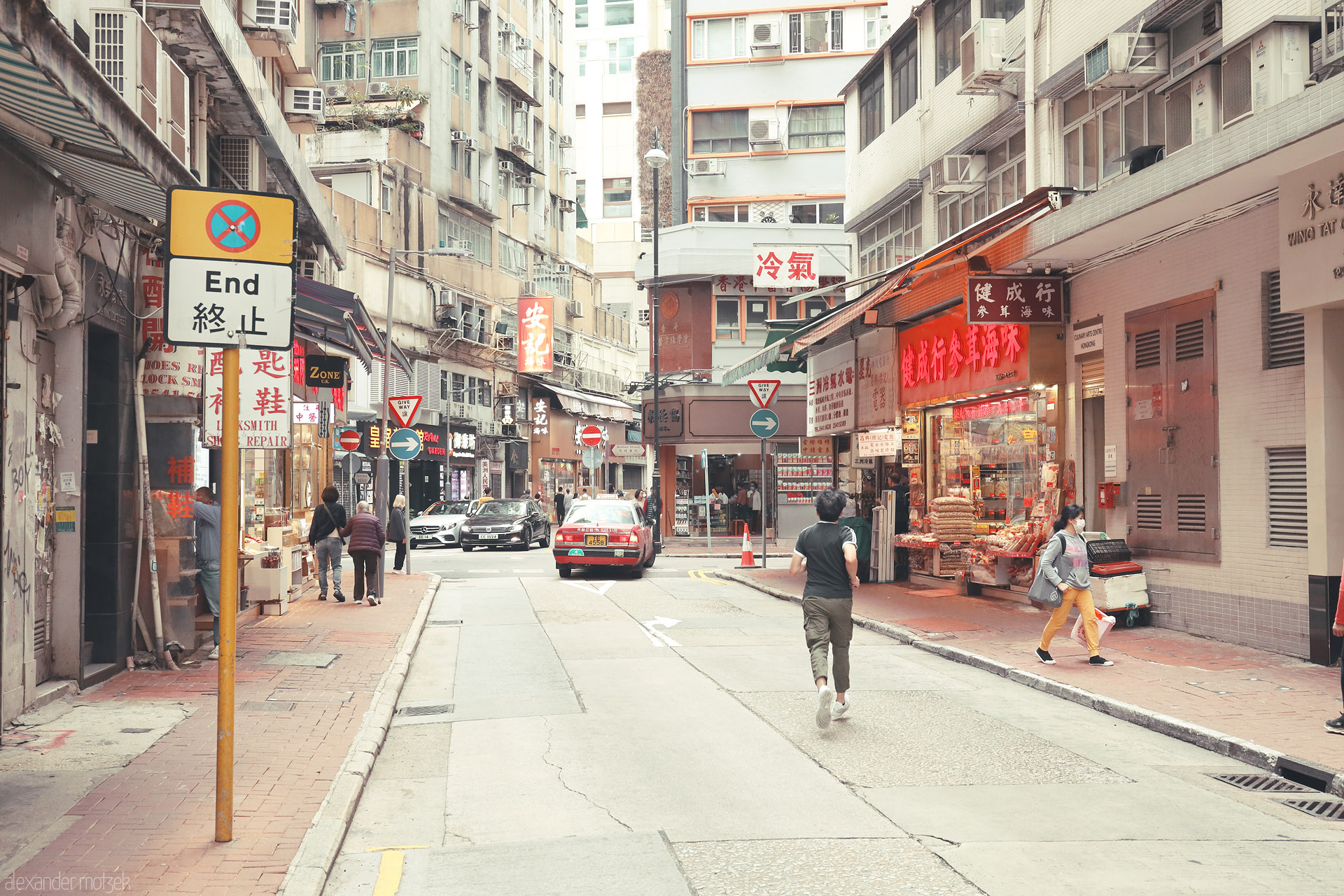 Foto von Pedestrians and a red taxi pass old shopfronts and Cantonese signs on a narrow street in Hong Kong Island, Hong Kong.