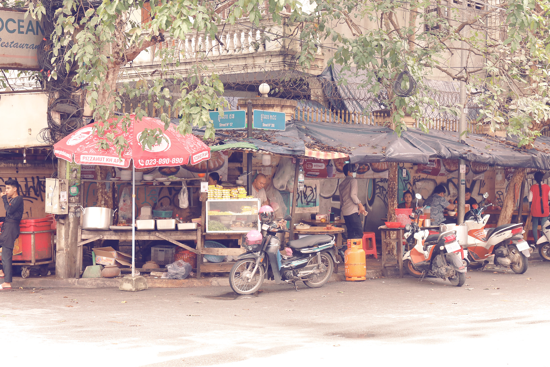Foto von Local street food stalls bustle under leafy shade, scooters parked in vibrant Phnom Penh, Cambodia, on bustling Street 136.