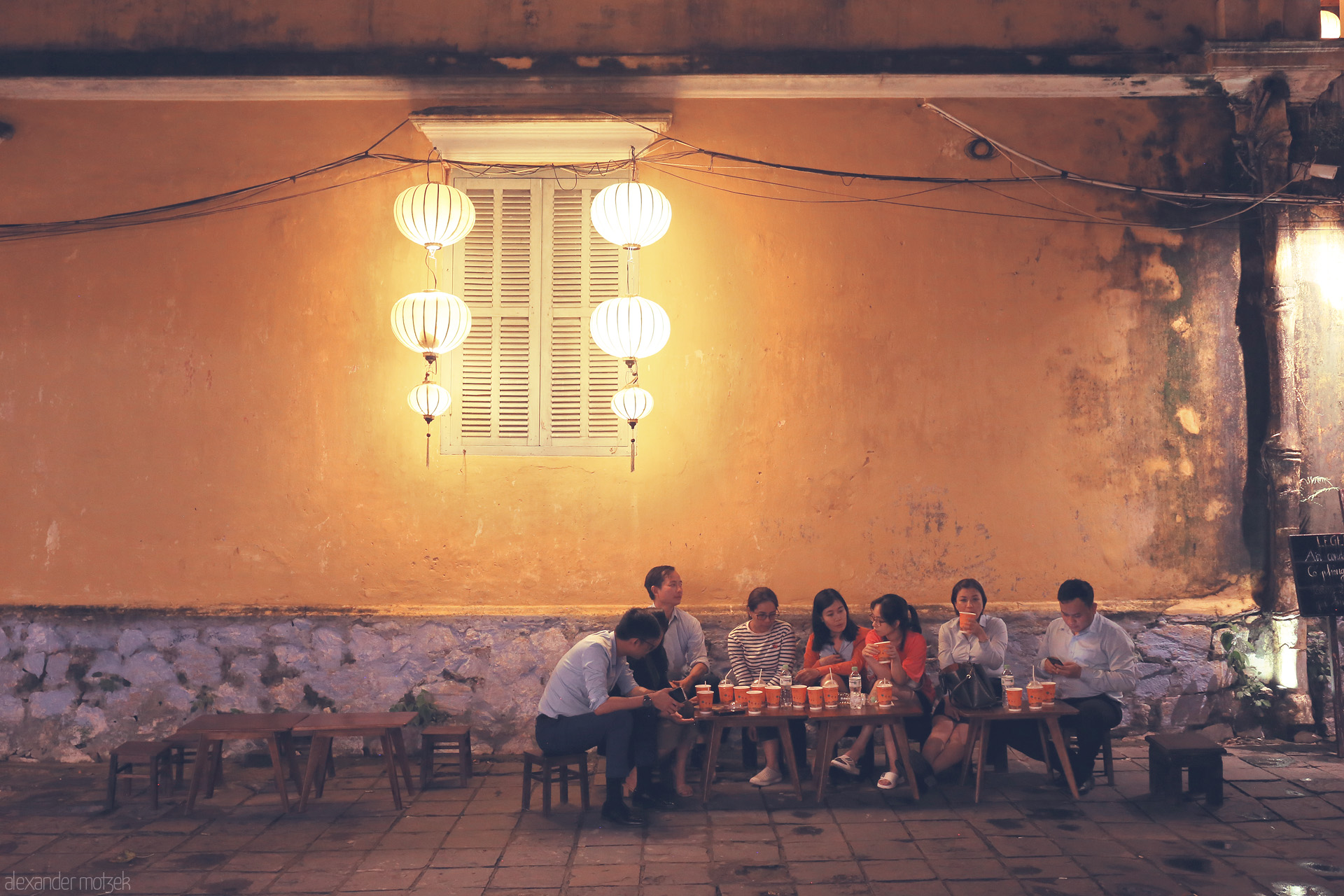 Foto von Locals savor street food under glowing lanterns, old town vibes radiating from a golden wall in Hoi An, Vietnam.