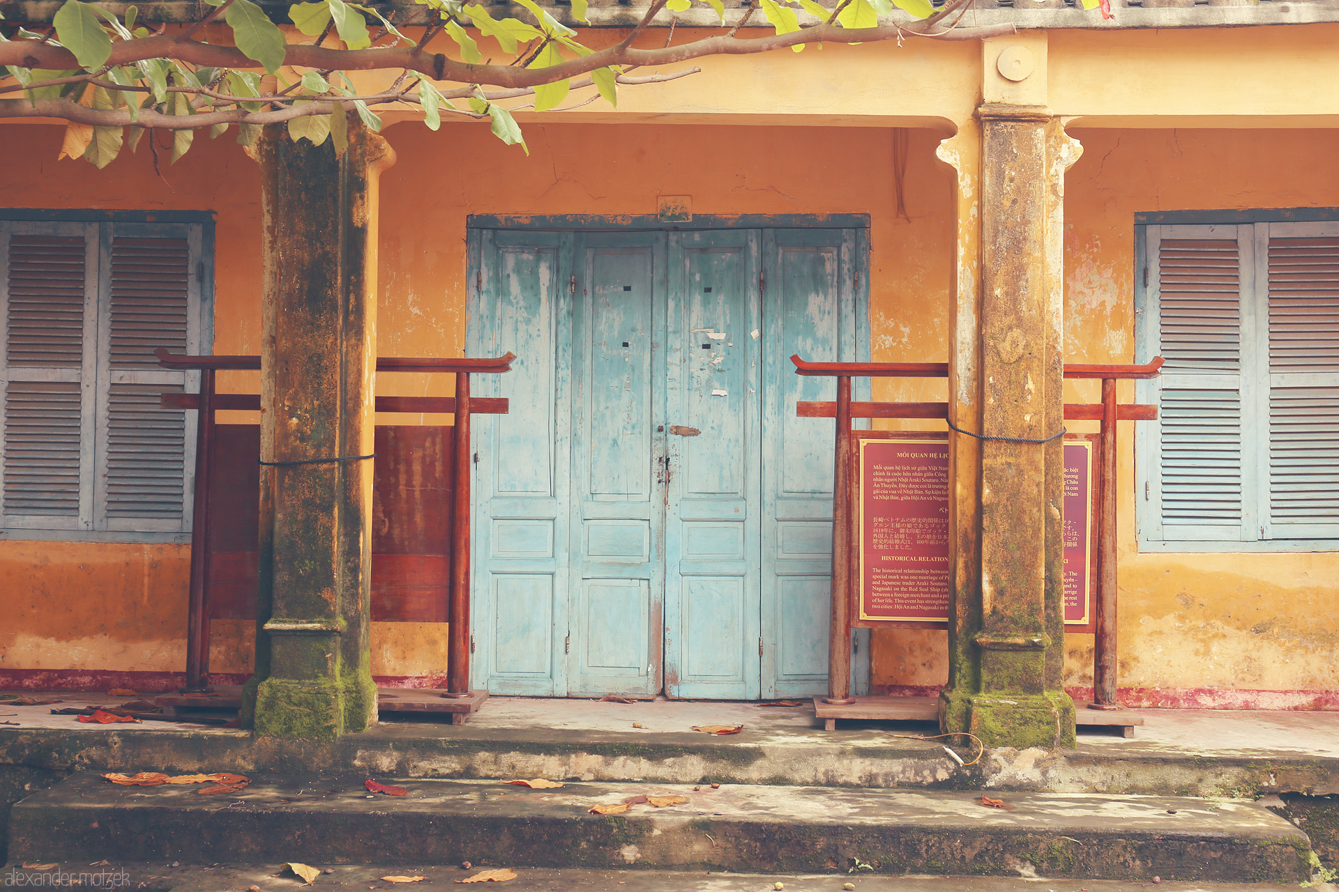 Foto von Moss-draped columns and faded blue doors in Hoi An, Vietnam evoke tranquil tales of history and time.