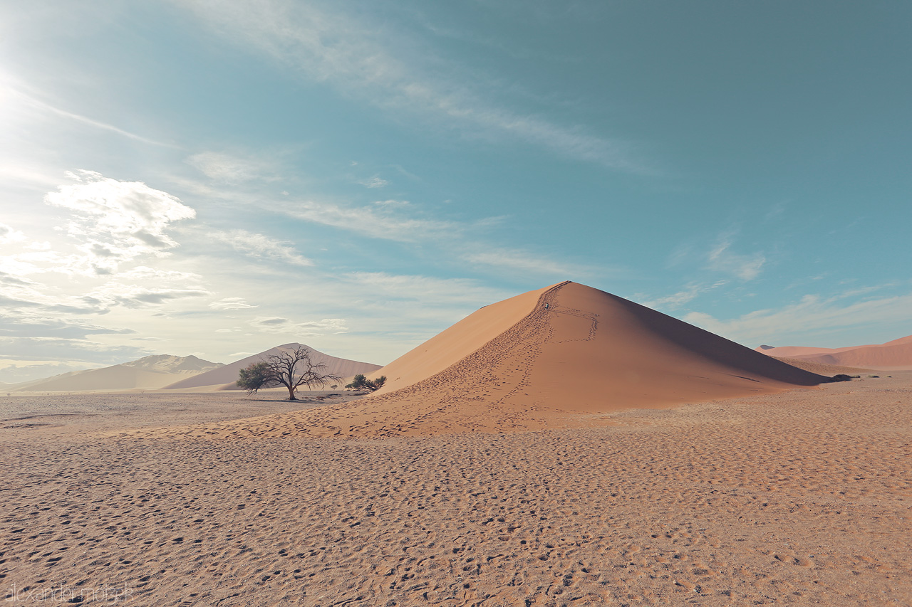 Foto von The serene sweep of a sand dune cast under the wide Namibian sky, footprints charting an ephemeral journey.