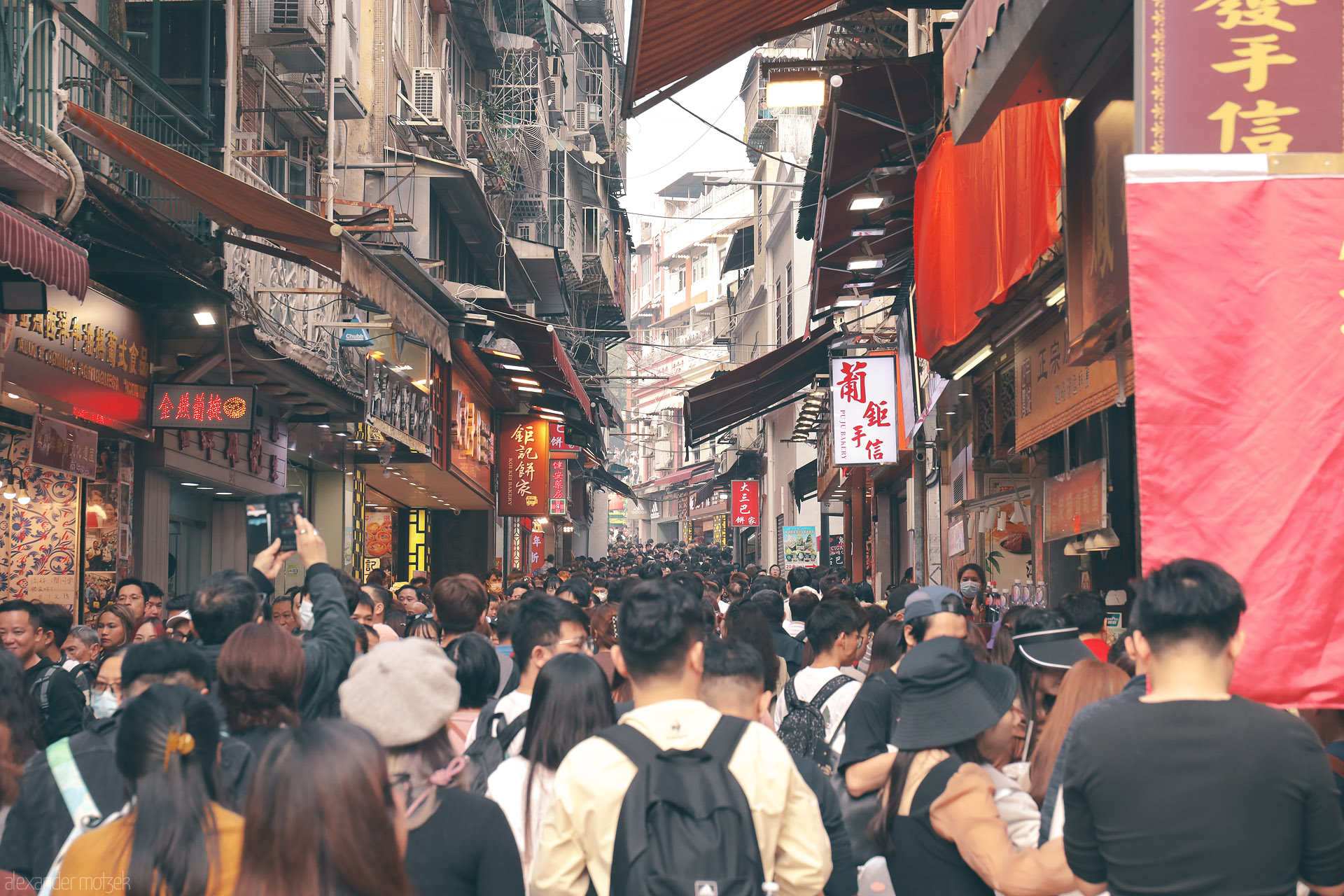 Foto von Packed Taipa lane in Macau, a sea of visitors beneath awnings and bright Chinese shop signs, soaking up the old-town bustle.