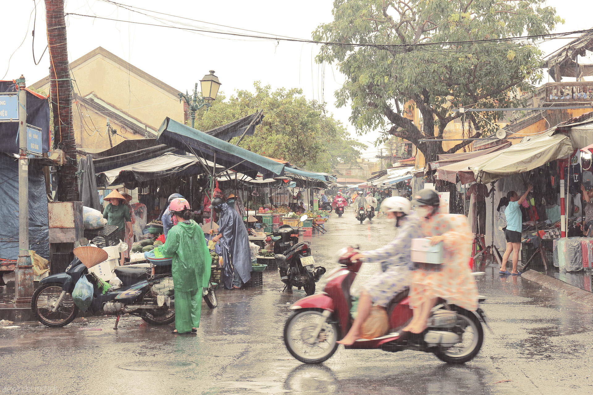 Foto von Rain-soaked Hoi An market bustles as locals in ponchos and conical hats trade and zip by on scooters—Vietnamese life in poetic motion.