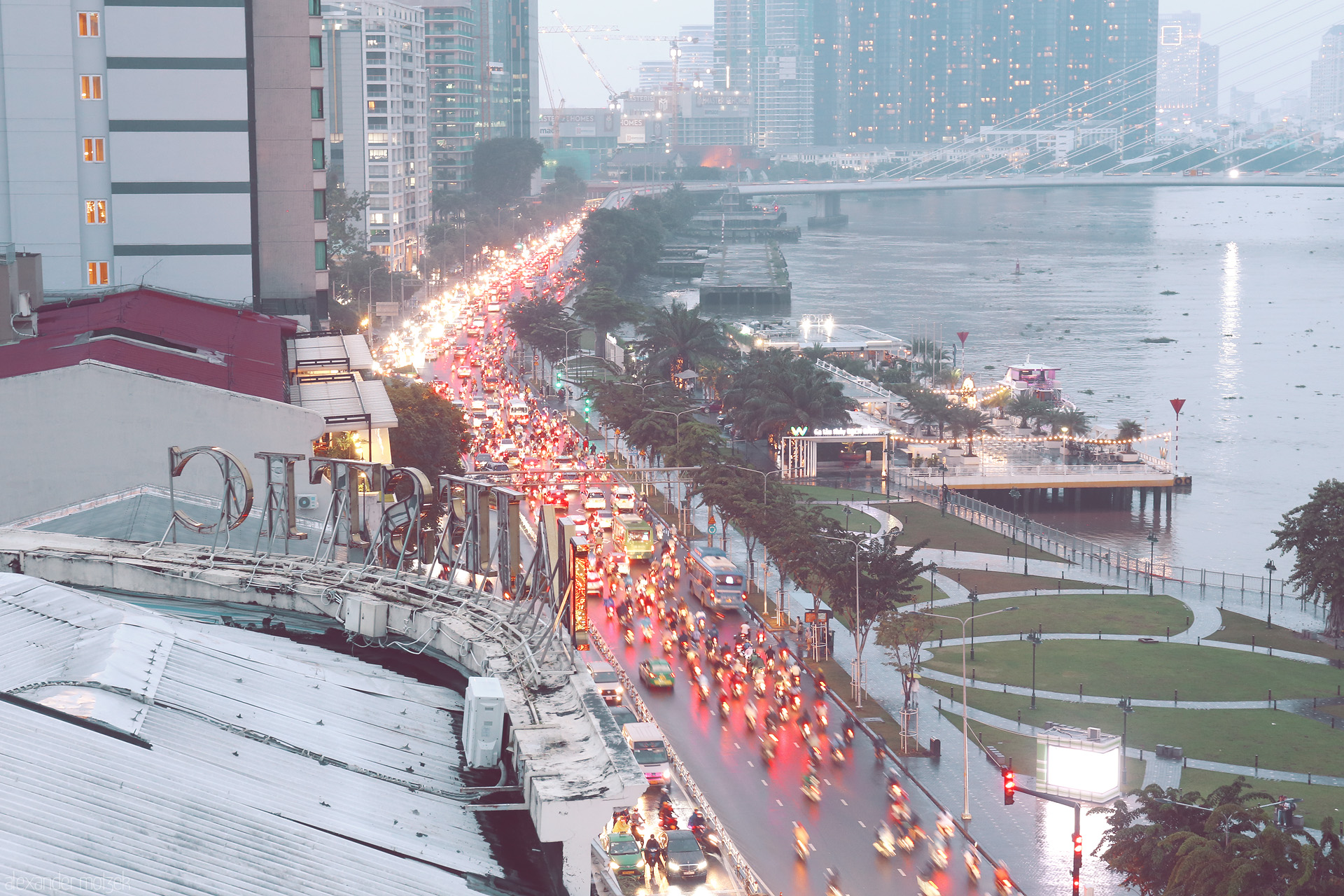 Foto von Rush hour veils Saigon’s Bach Dang riverside in lights, where dỏ xe máy flow beside the tranquil Sông Sài Gòn, city pulse meets water calm.