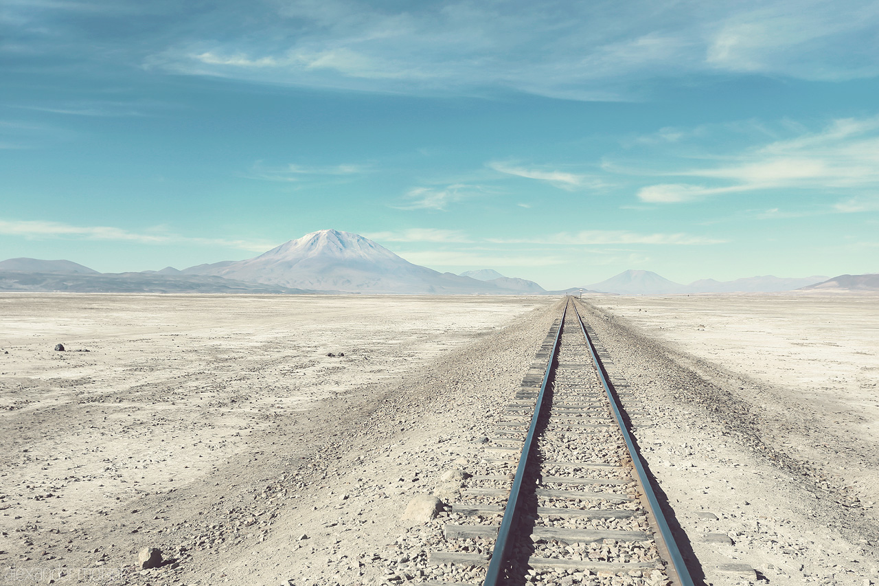 Tracks Foto von Schienen in der Salzwüste Salar de Uyuni in Bolivien mit hohem Vulkan im Hintergrund