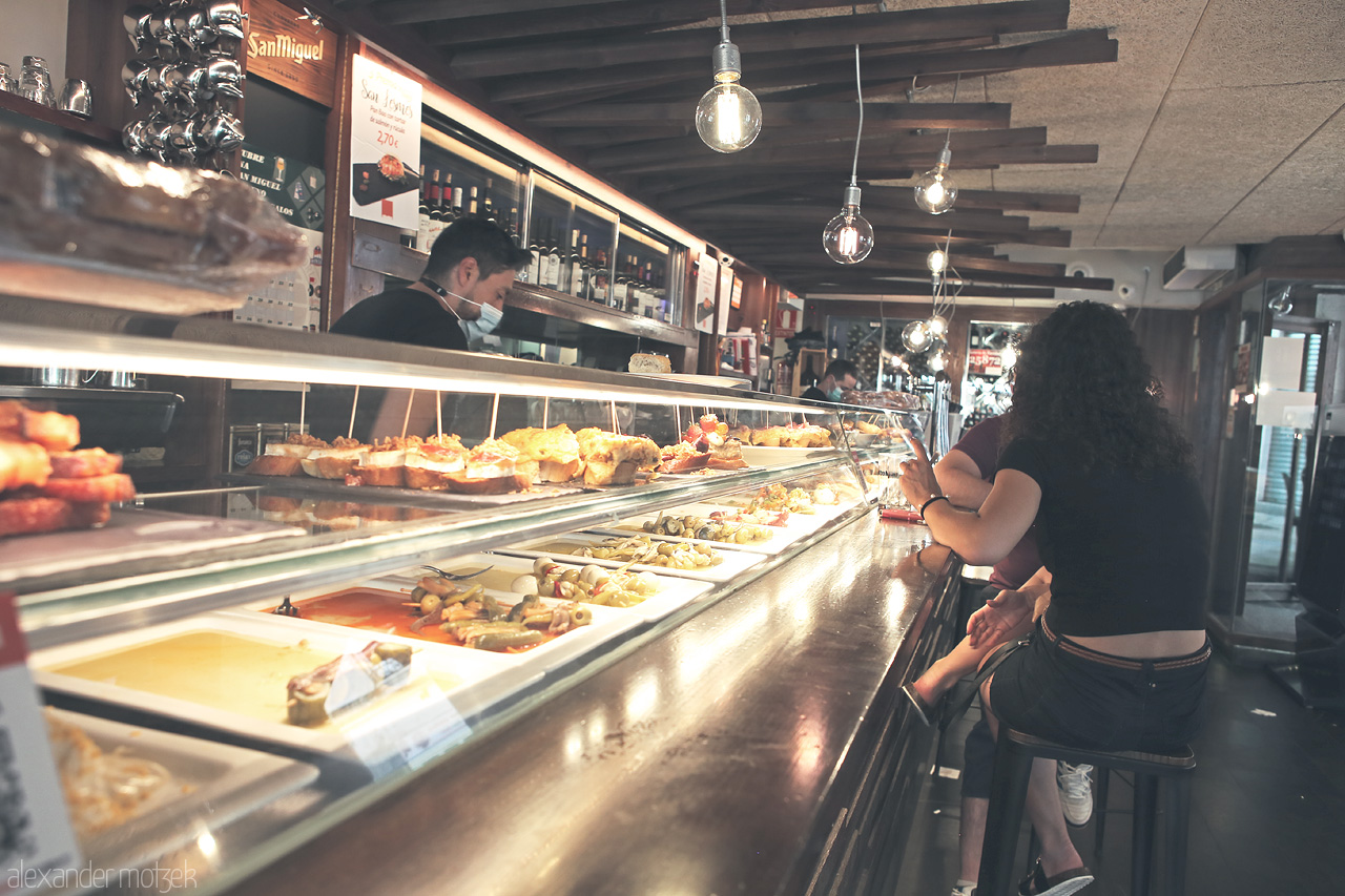 Foto von Patrons at a bar in Burgos, enjoying traditional Basque pintxos under warm ambient light.