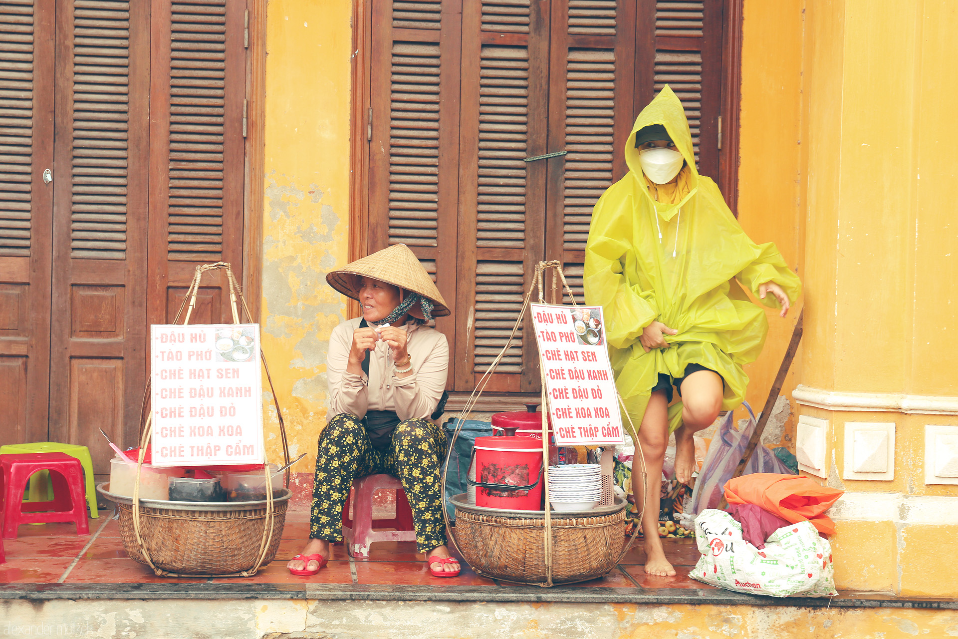 Foto von Streetside chè sellers pause on a rainy day, yellow ancient walls of Hoi An framing everyday life and local flavors.