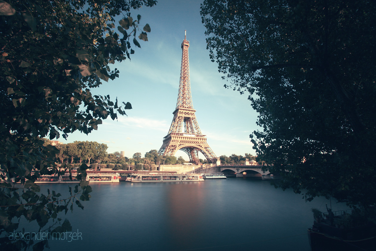 Seine Serenity Foto von The Eiffel Tower majestically rises beside the serene waters of the Seine, framed by lush trees on a tranquil Parisian day.